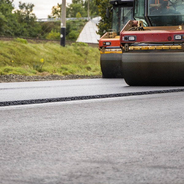 Heavy road rollers compacting fresh asphalt layer on road. Concept of infrastructure, civil engineering, road maintenance, road building, and construction machinery.